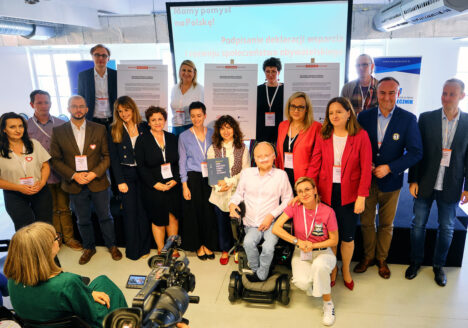 Grupa kilkunastu osób pozuje do zdjęcia. Na pierwszym planie widać nagrywającą ich kamerę. Za nimi widać tablice z wydrukami deklaracji współpracy w dużym formacie, a w tle duży ekran z wyświetlanym przez rzutnik hasłem „Mamy pomysł na Polskę! Podpisanie deklaracji wsparcia i rozwoju społeczeństwa obywatelskiego”.