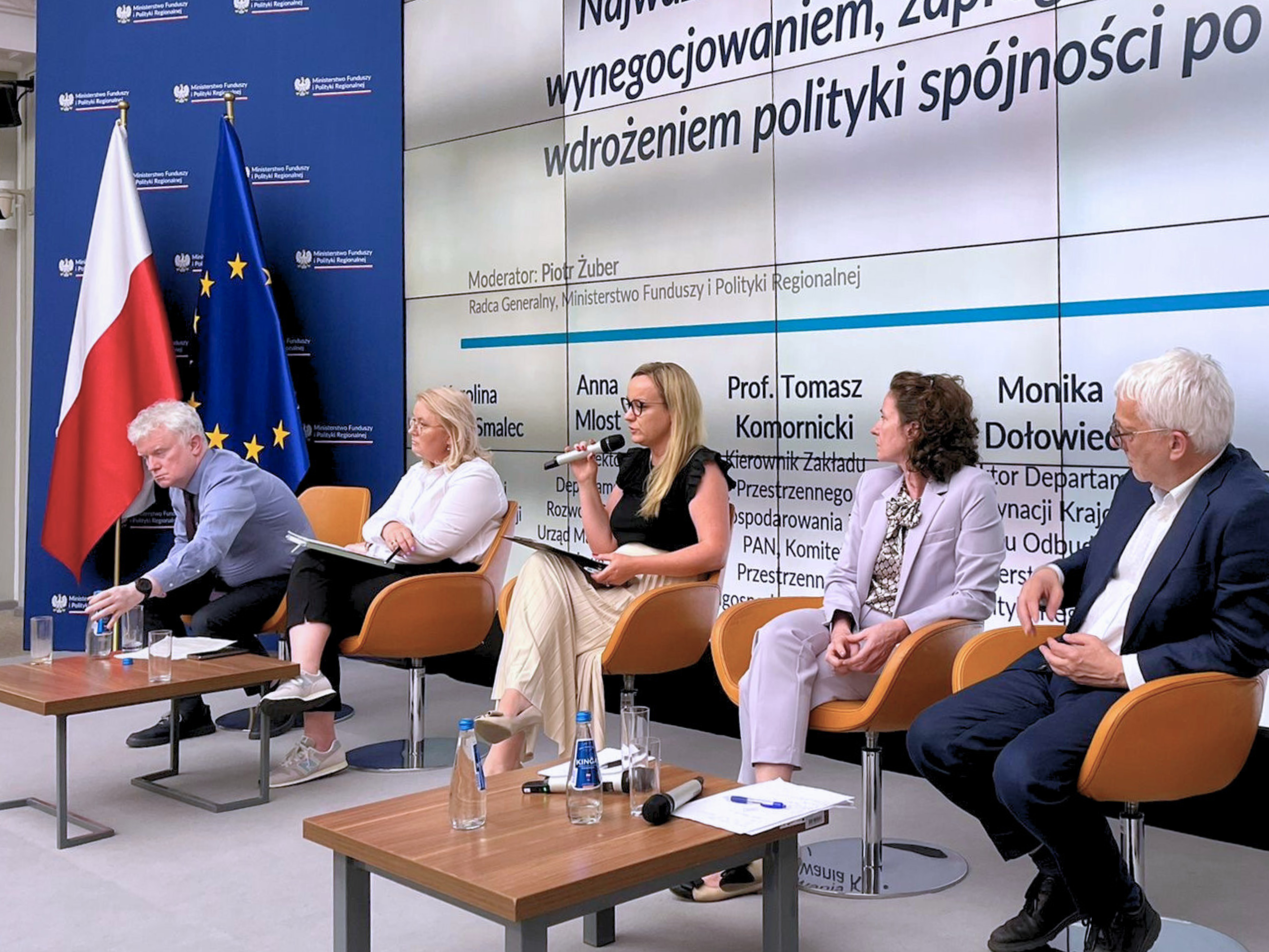Scena, cztery osoby siedzą na fotelach, jedna z nich trzyma mikrofon. Po lewej stronie ścianka MFiPR oraz flagi Polski i Unii Europejskiej. Za panelistami duży ekran, na którym w kadrze widać fragment tytułu panelu oraz imiona i nazwiska występujących. Przed panelistami dwa niewielkie stoliki z wodą, mikrofonami i notatkami.
